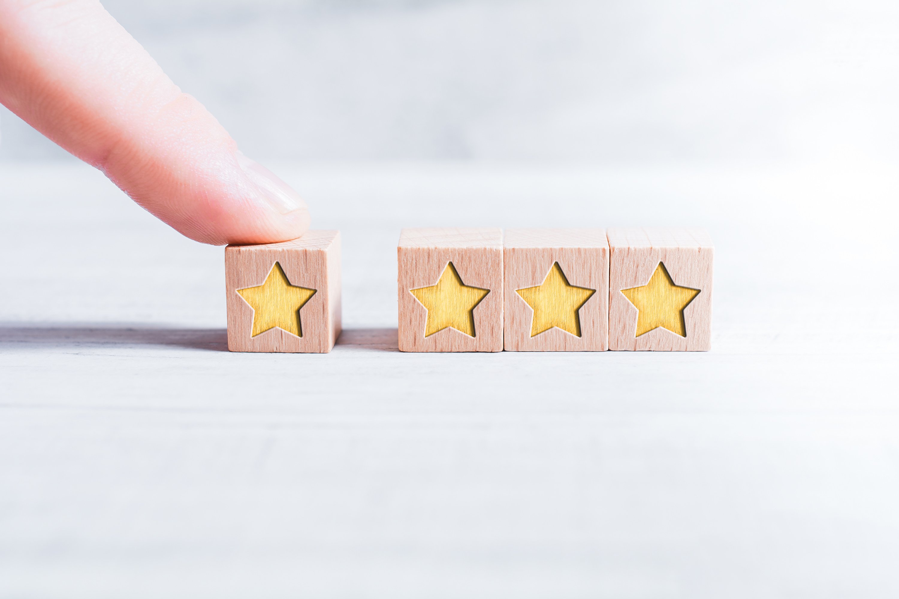 4 Star Rating Formed By Wooden Blocks And Arranged By A Male Finger On A White Table